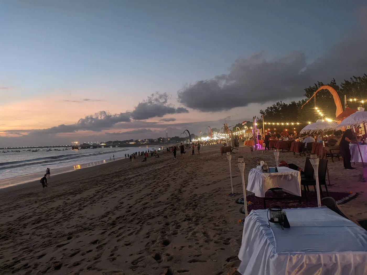 Dinner tables set up in the sand at a Jimbaran beach restaurant at sunset