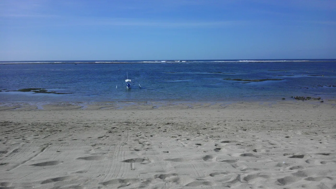 The calm, reef-sheltered turquoise shallows and pale sand of a Nusa Dua beach