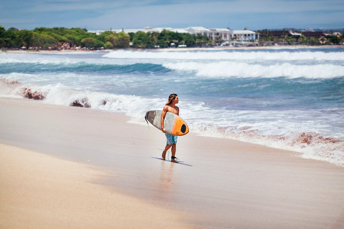 A surfer carrying his board along the sand at Kuta Beach, south Bali