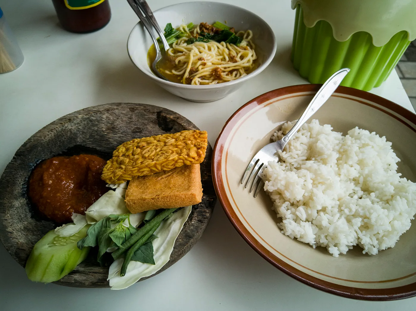 A simple warung plate of rice, tempeh, tofu, sambal and vegetables with noodle soup