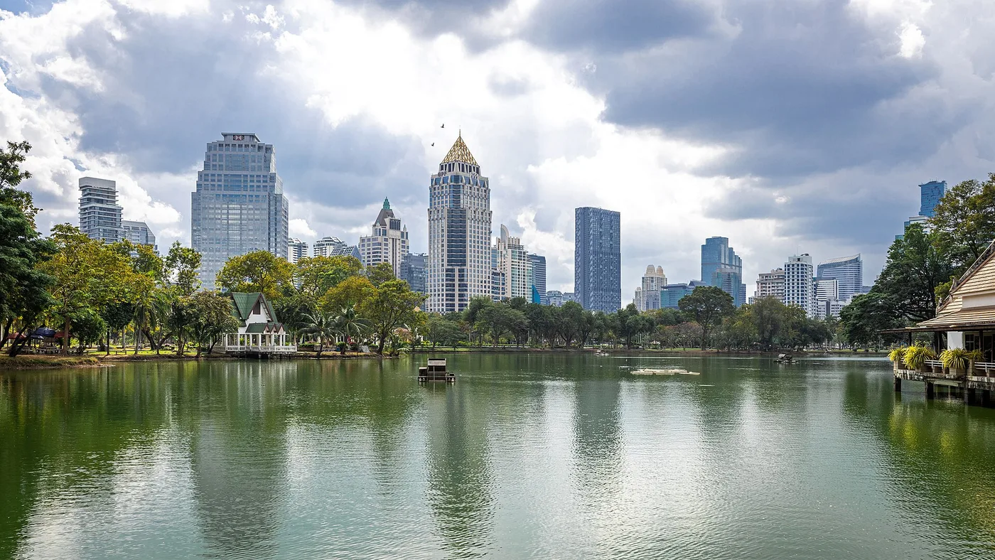 Lumphini Park's lake and pavilions with the Bangkok skyline behind