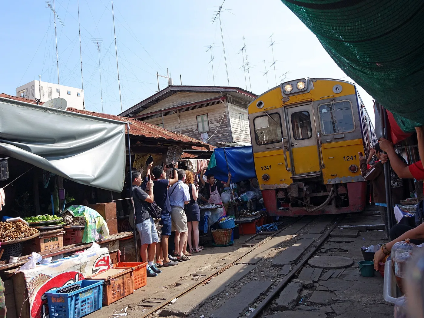 A train rolling past market stalls with their awnings folded back at Maeklong Railway Market