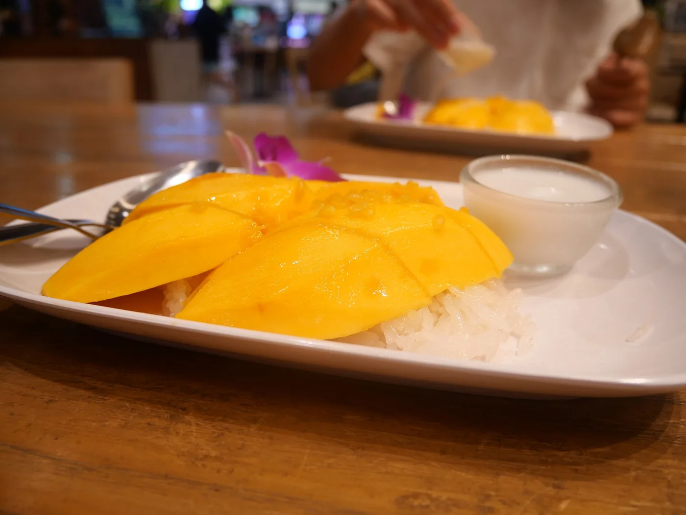 A plate of mango sticky rice with a cup of coconut sauce