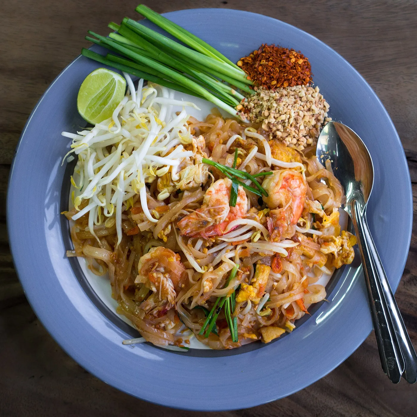 A plate of prawn pad thai with lime, bean sprouts, peanuts and chilli