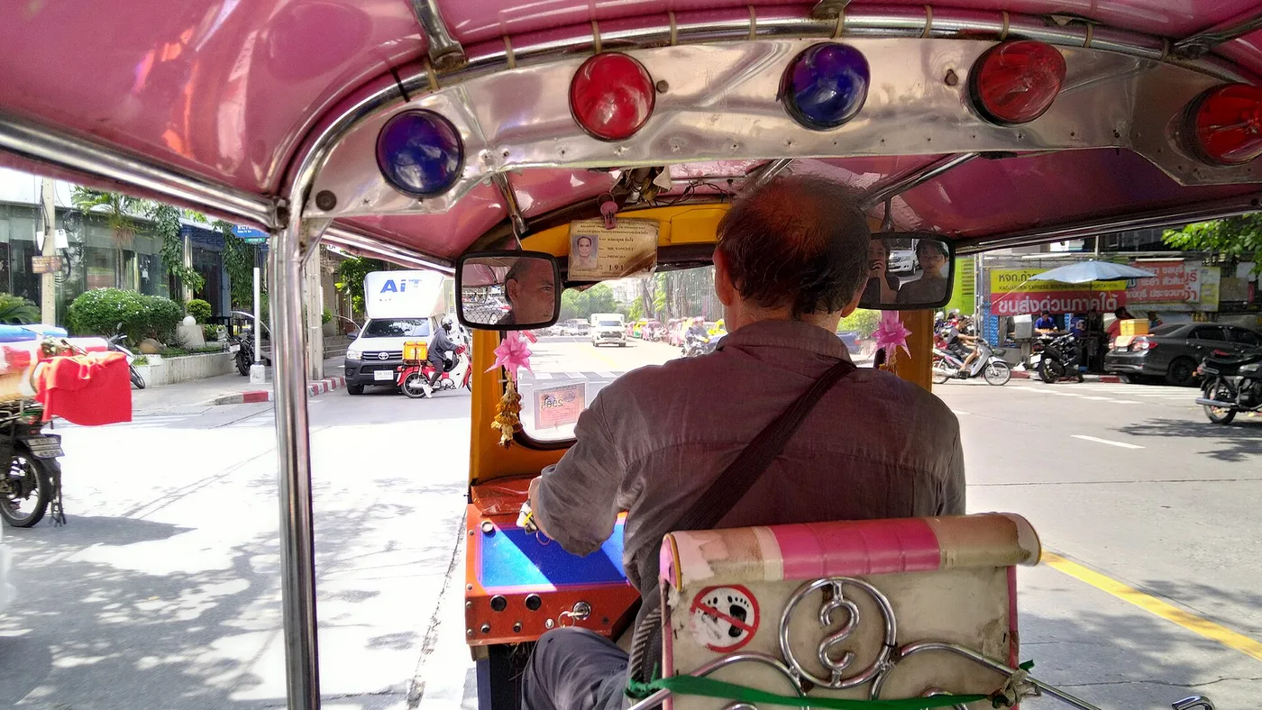 The view from inside a pink tuk-tuk riding through Bangkok traffic