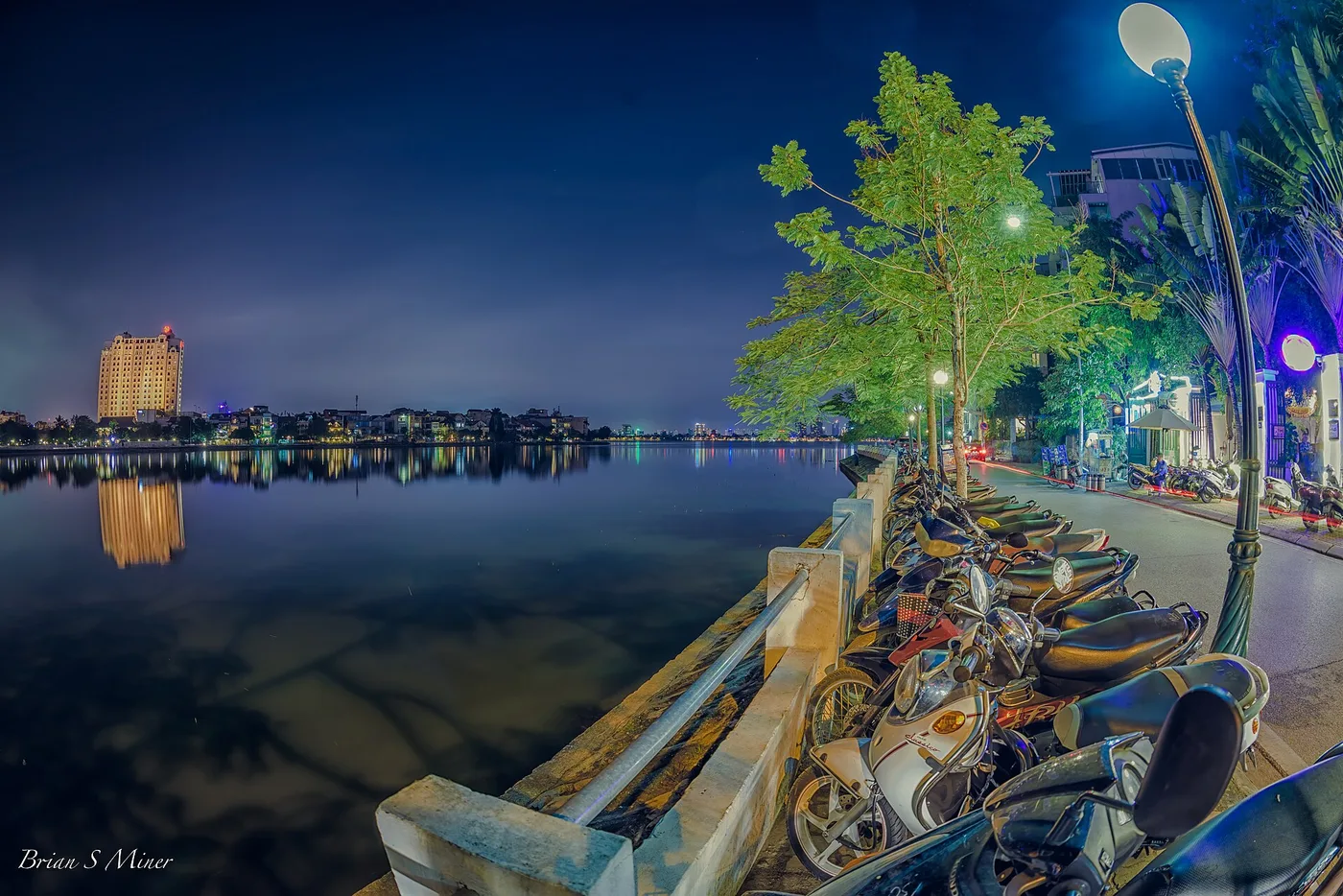 Motorbikes and scooters parked along a lakeside promenade in Hanoi at night