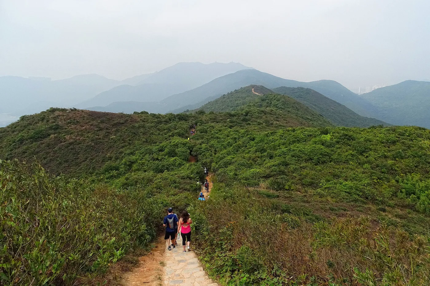 Hikers on the Dragon's Back ridge trail above the green hills