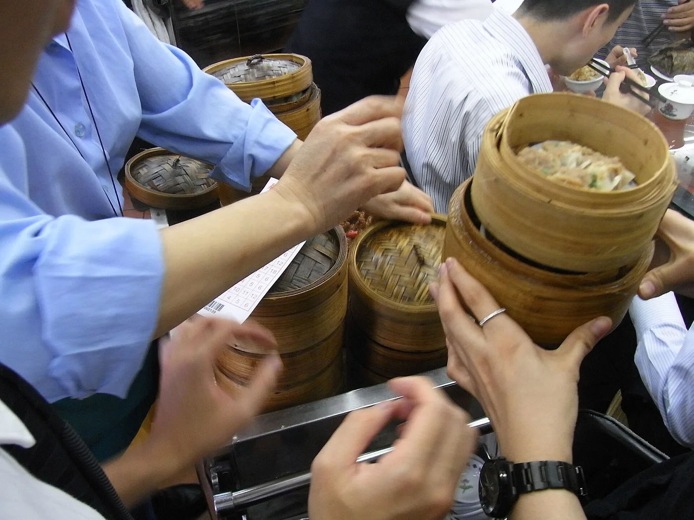 Diners reaching for stacked bamboo steamers on a cart at an old Hong Kong tea house