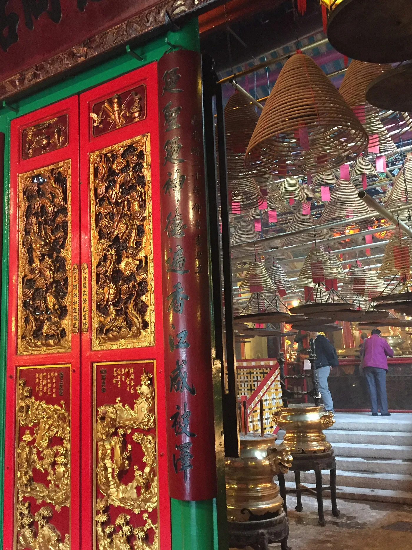 Ornate red-and-gold temple doors beside hanging spiral incense coils at Man Mo Temple