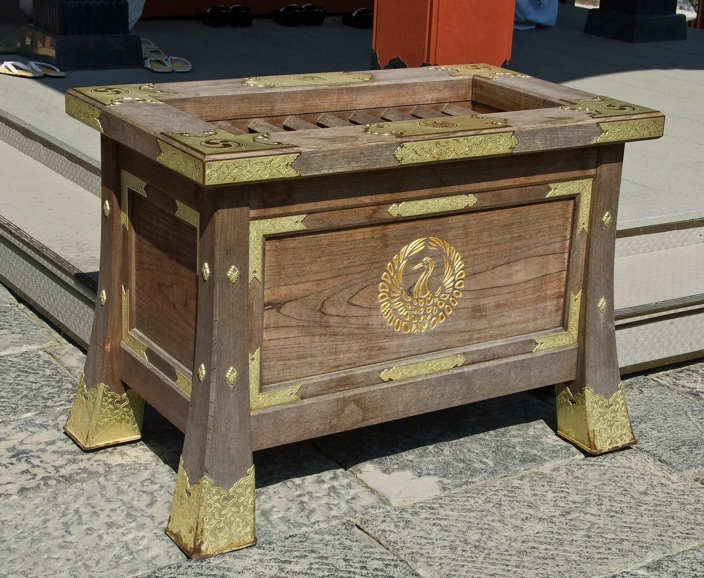 A wooden Shinto offering box, the saisen-bako, with brass fittings and a gold crane crest at a shrine