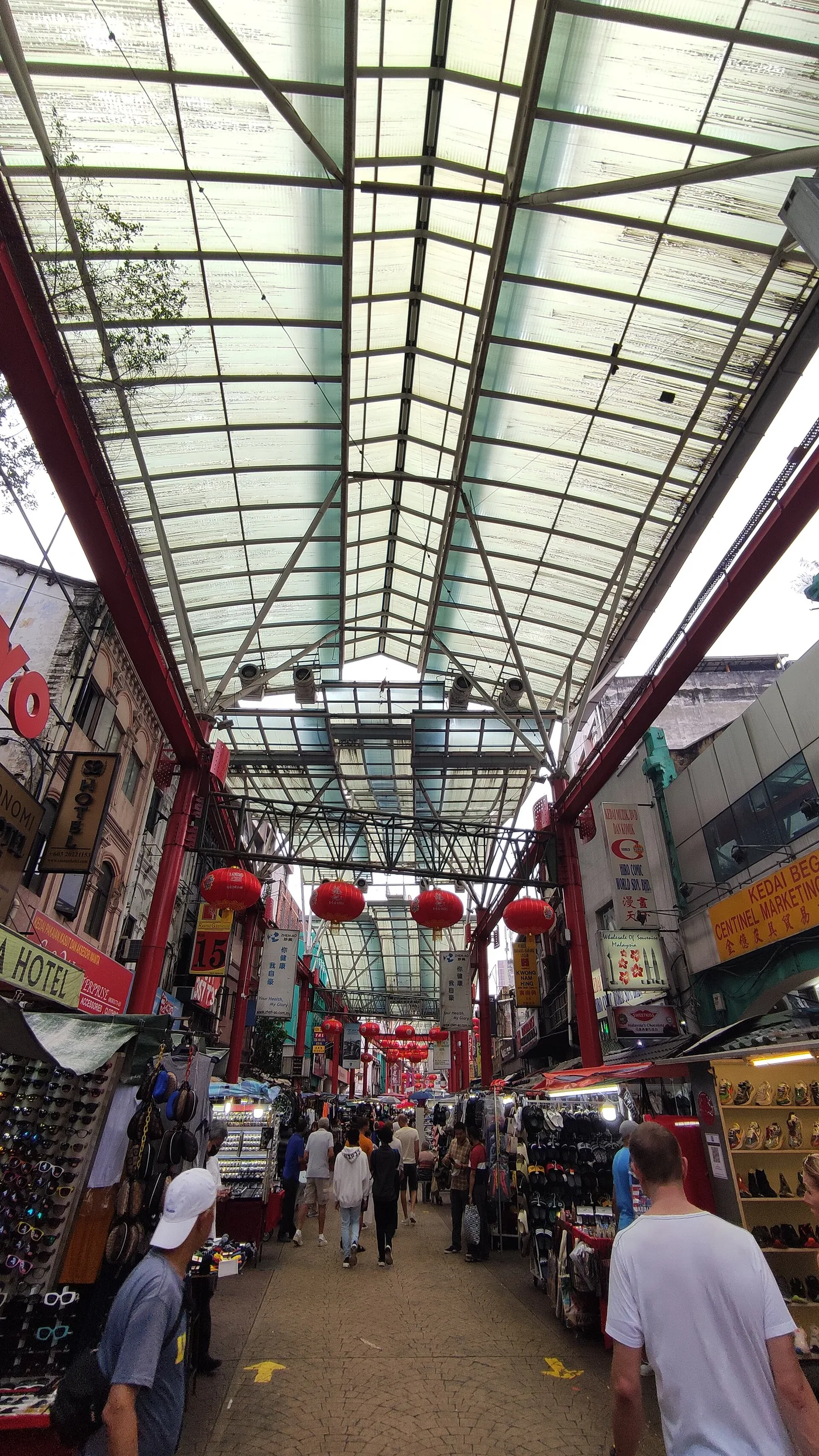 The covered, lantern-hung market lane of Petaling Street, stalls either side and shoppers walking through
