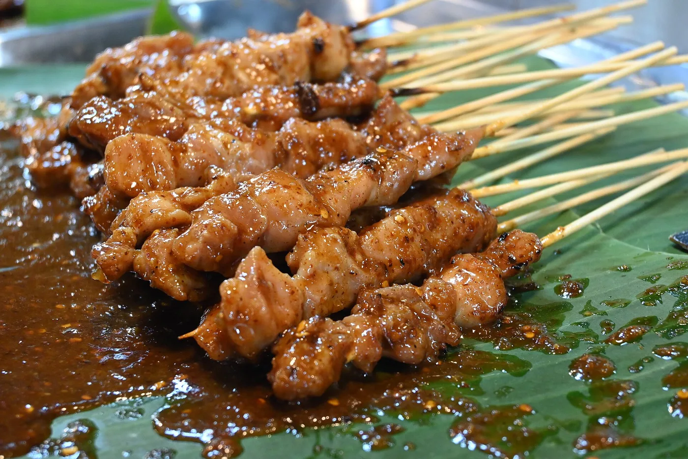 Char-grilled satay skewers glazed in peanut sauce on a banana leaf