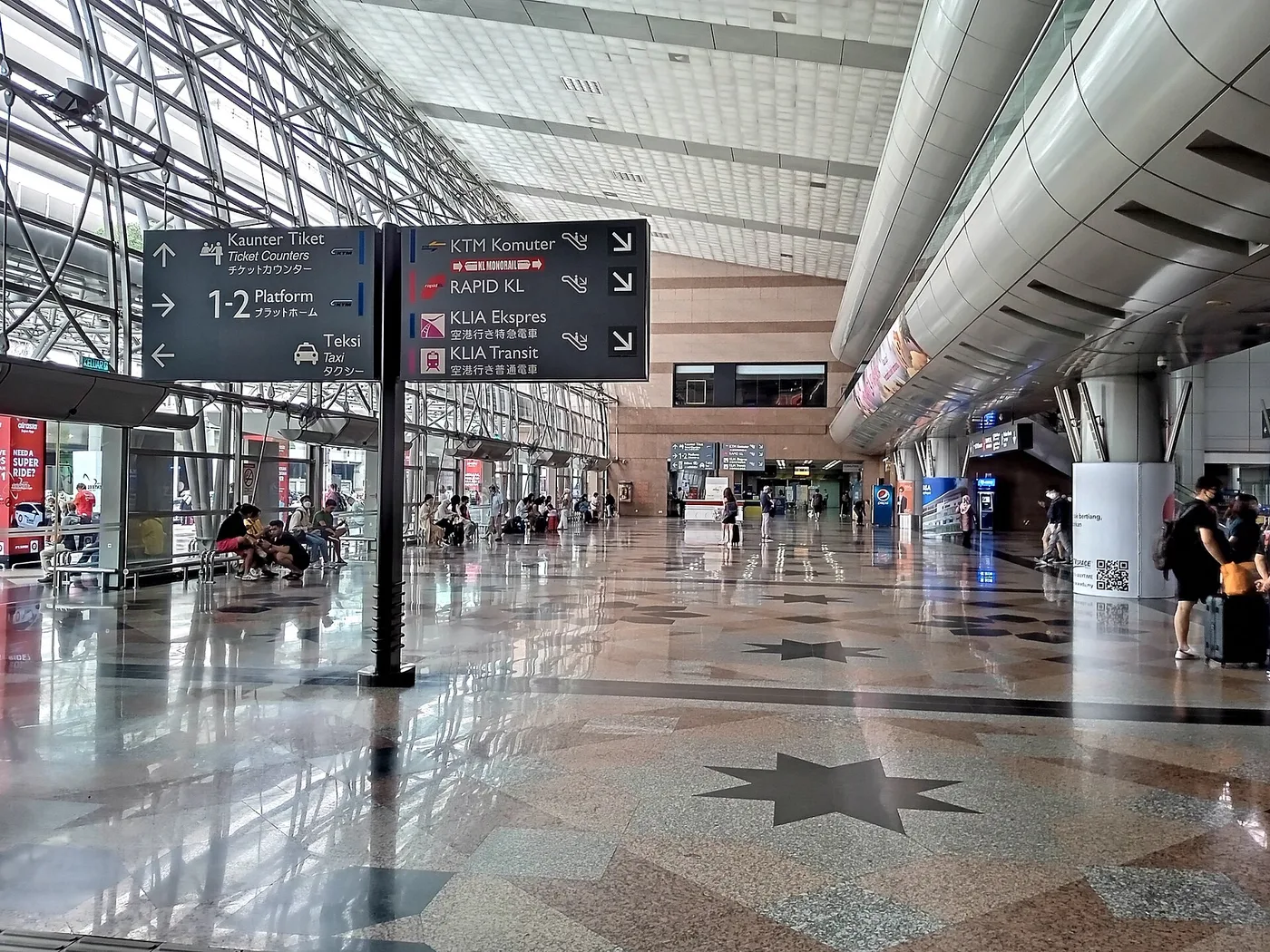 KL Sentral's ticket hall, overhead signage pointing to KTM Komuter, the Monorail, Rapid KL and the KLIA Ekspres