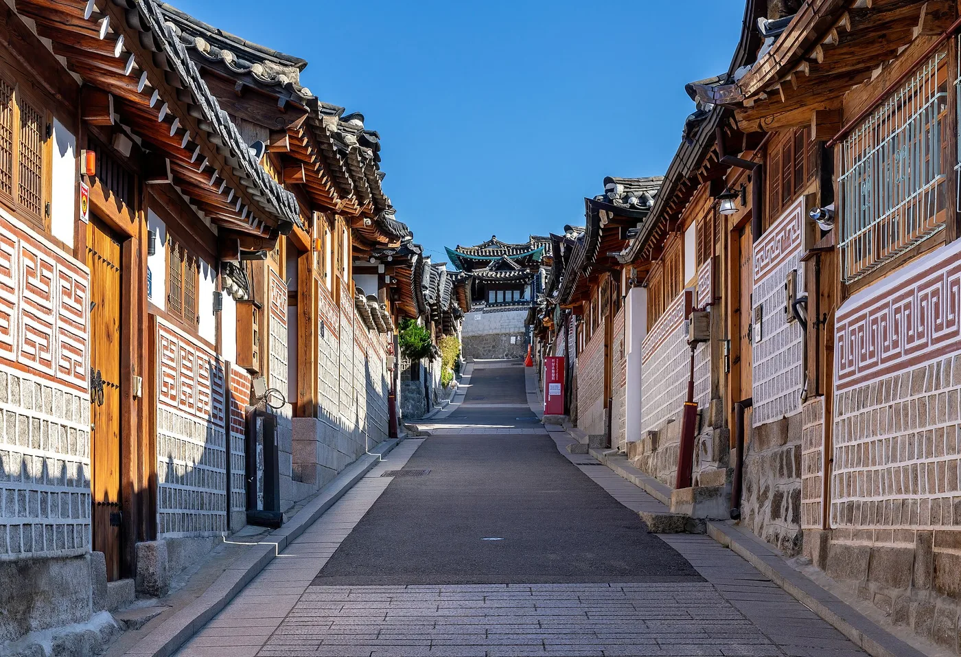 A quiet stone-paved lane climbing through Bukchon Hanok Village, tiled hanok roofs on both sides