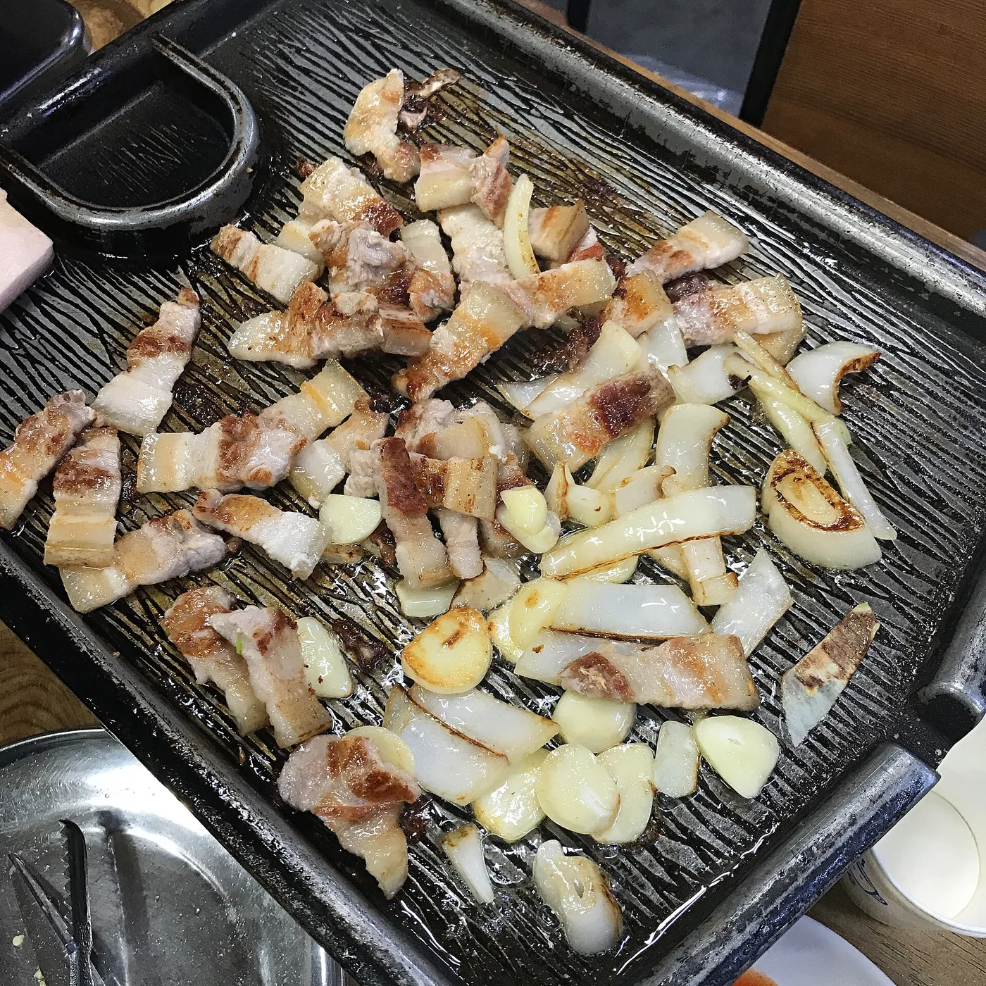 Strips of pork belly and sliced onion grilling on a ridged tabletop grill