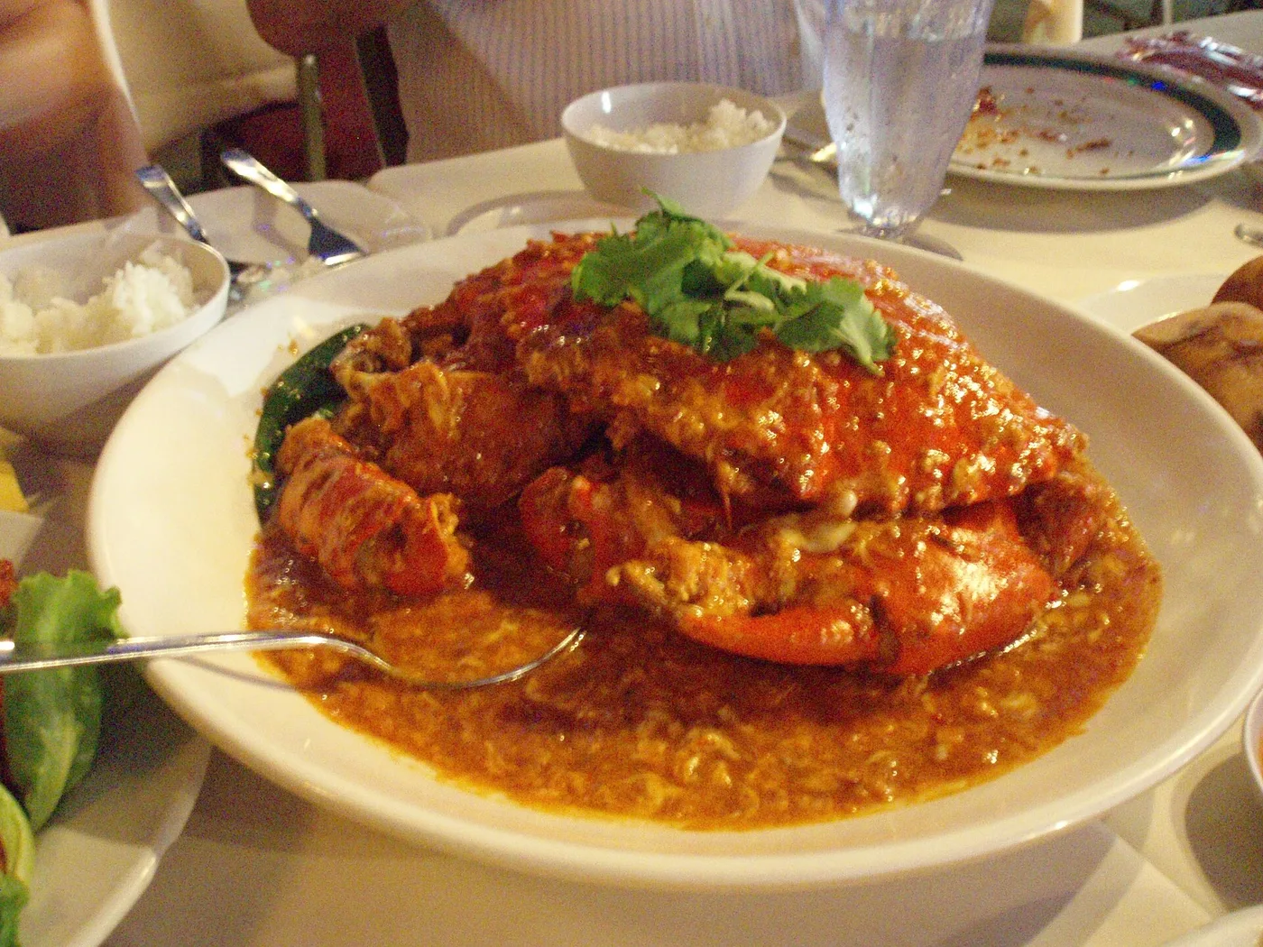 A whole chilli crab in red gravy, topped with cilantro, beside a bowl of rice