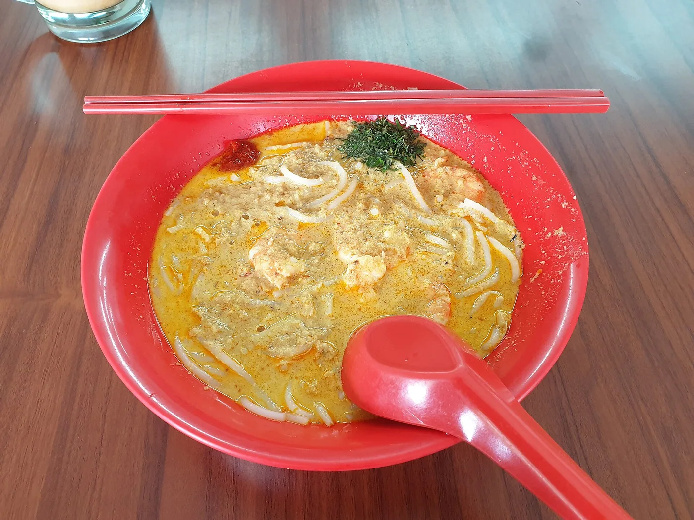 A red bowl of Katong laksa — coconut-curry broth, rice noodles and prawns
