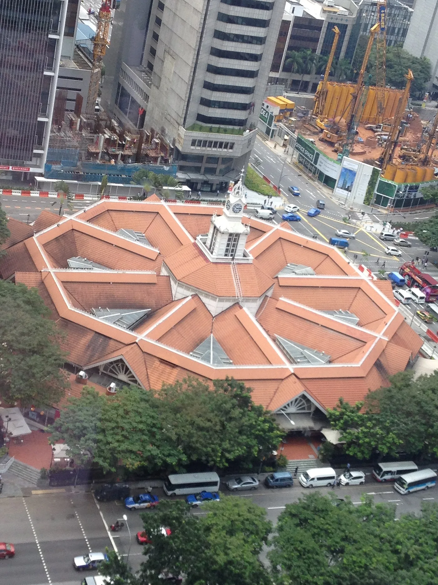 An aerial view of Lau Pa Sat's octagonal Victorian market hall and clock tower, ringed by CBD skyscrapers