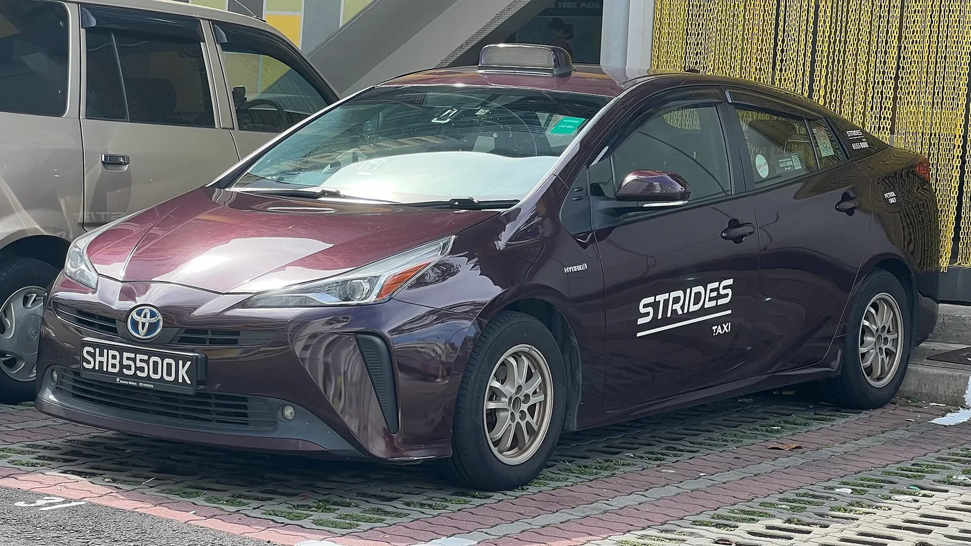 A maroon Strides Taxi, one of Singapore's licensed street taxis, parked at a kerb