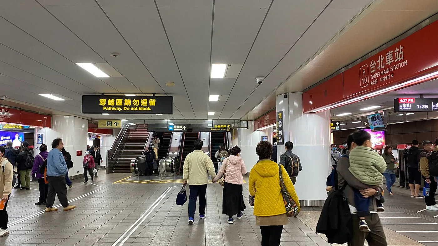 A concourse at Taipei Main Station with bilingual signage and escalators