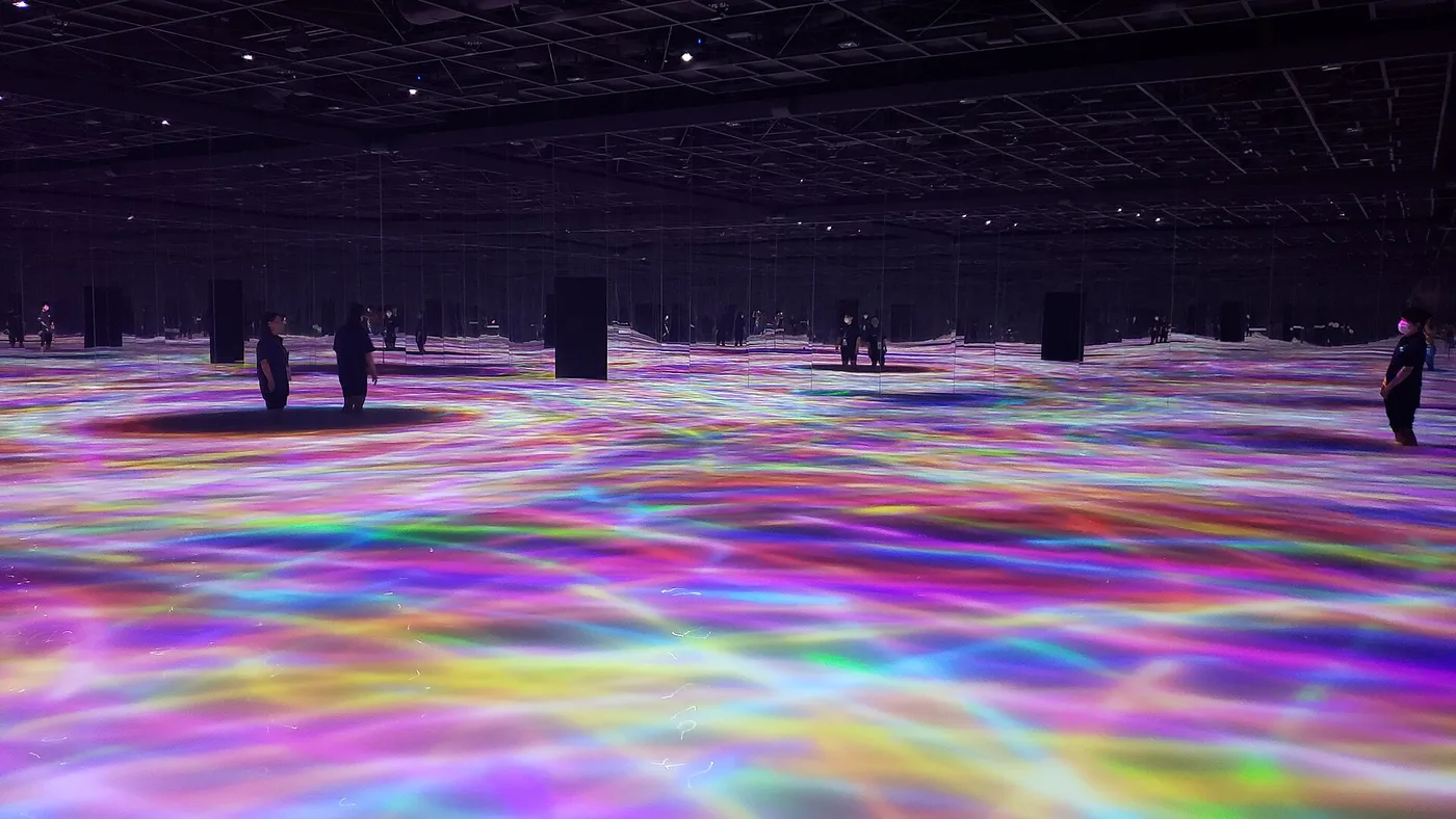 Visitors wading through knee-deep water under projected colour at teamLab Planets
